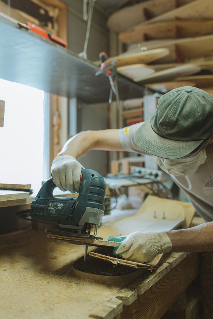A craftsman skillfully uses a jigsaw to create a skateboard in a home workshop.